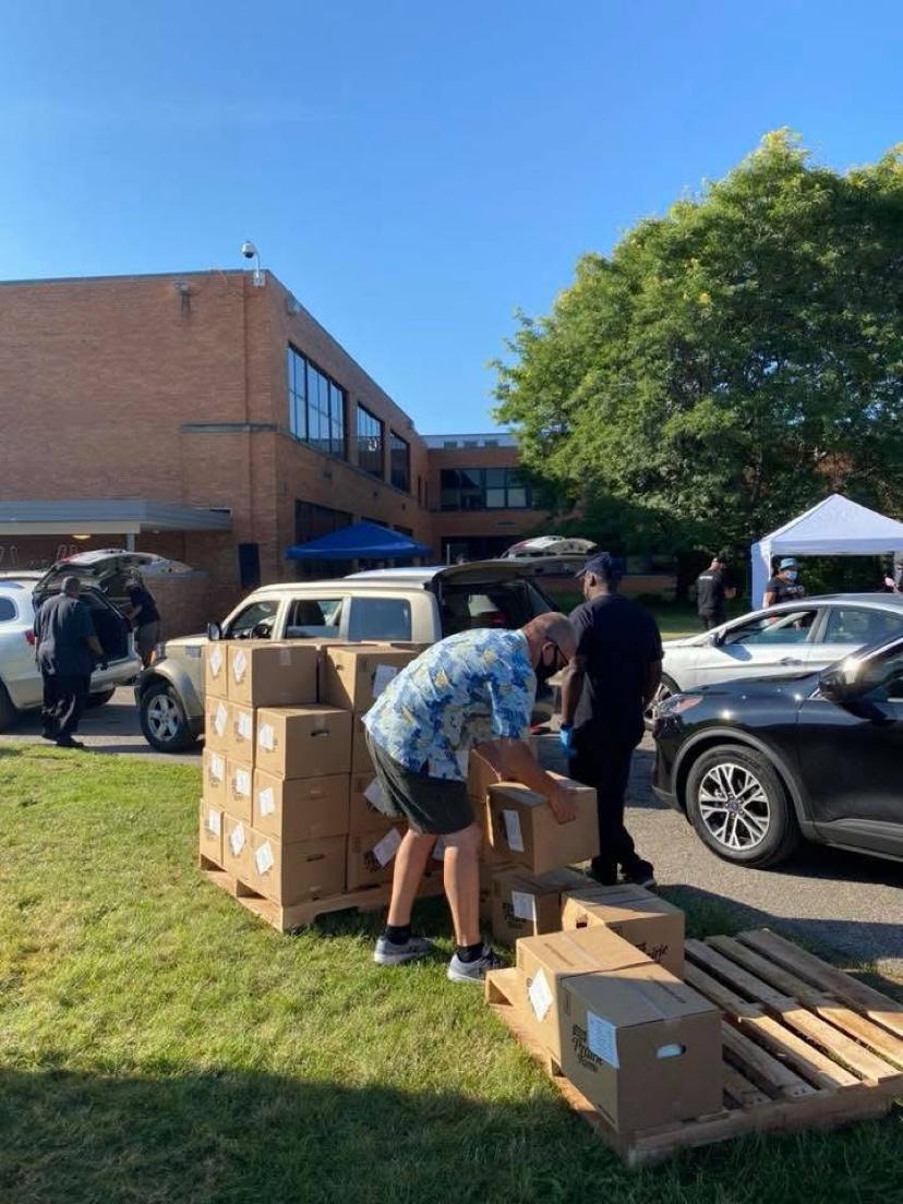 Volunteers stacking pallets of food boxes outdoors by parked cars