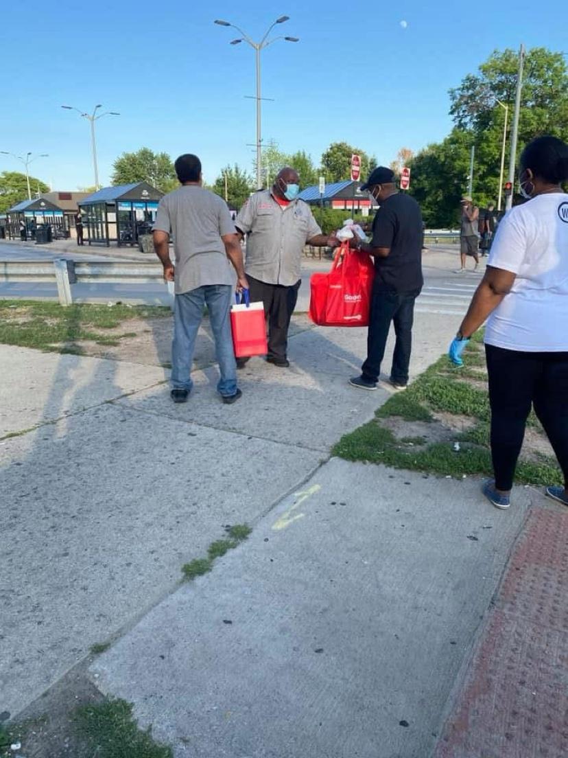 Volunteers handing red meal bags to men at an intersection